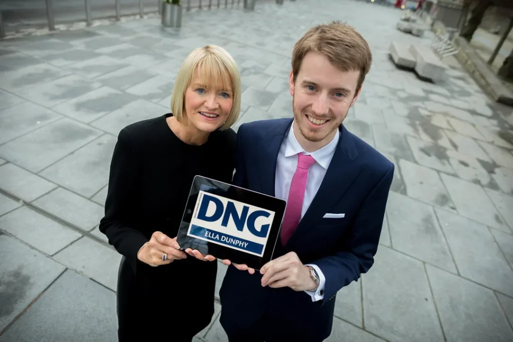 Two of the Ella Dunphy team smile, pose and hold a DNG Ella Dunphy sign