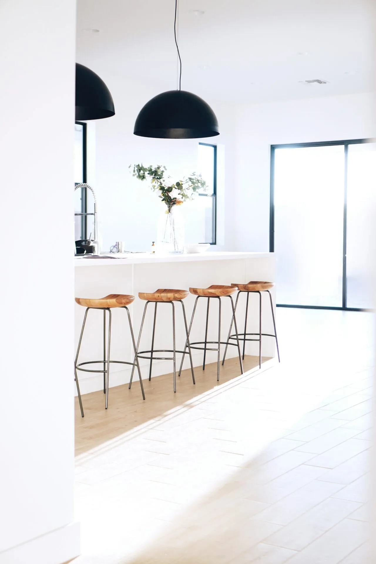 A bright kitchen with stools, a kitchen island and modern light fixtures