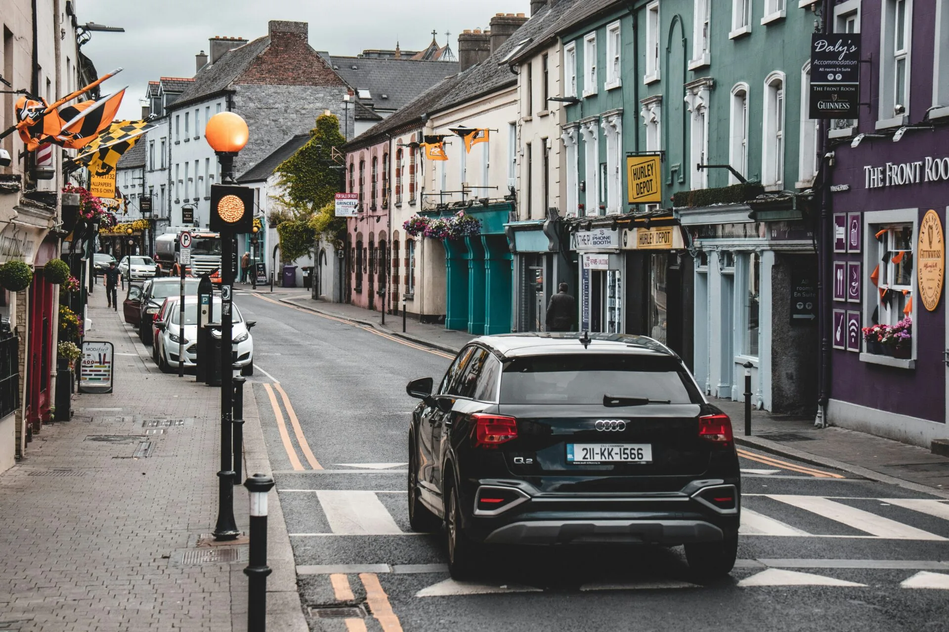 Kilkenny street featuring colourful shop fronts, a car, Kilkenny flas and streetlamps.