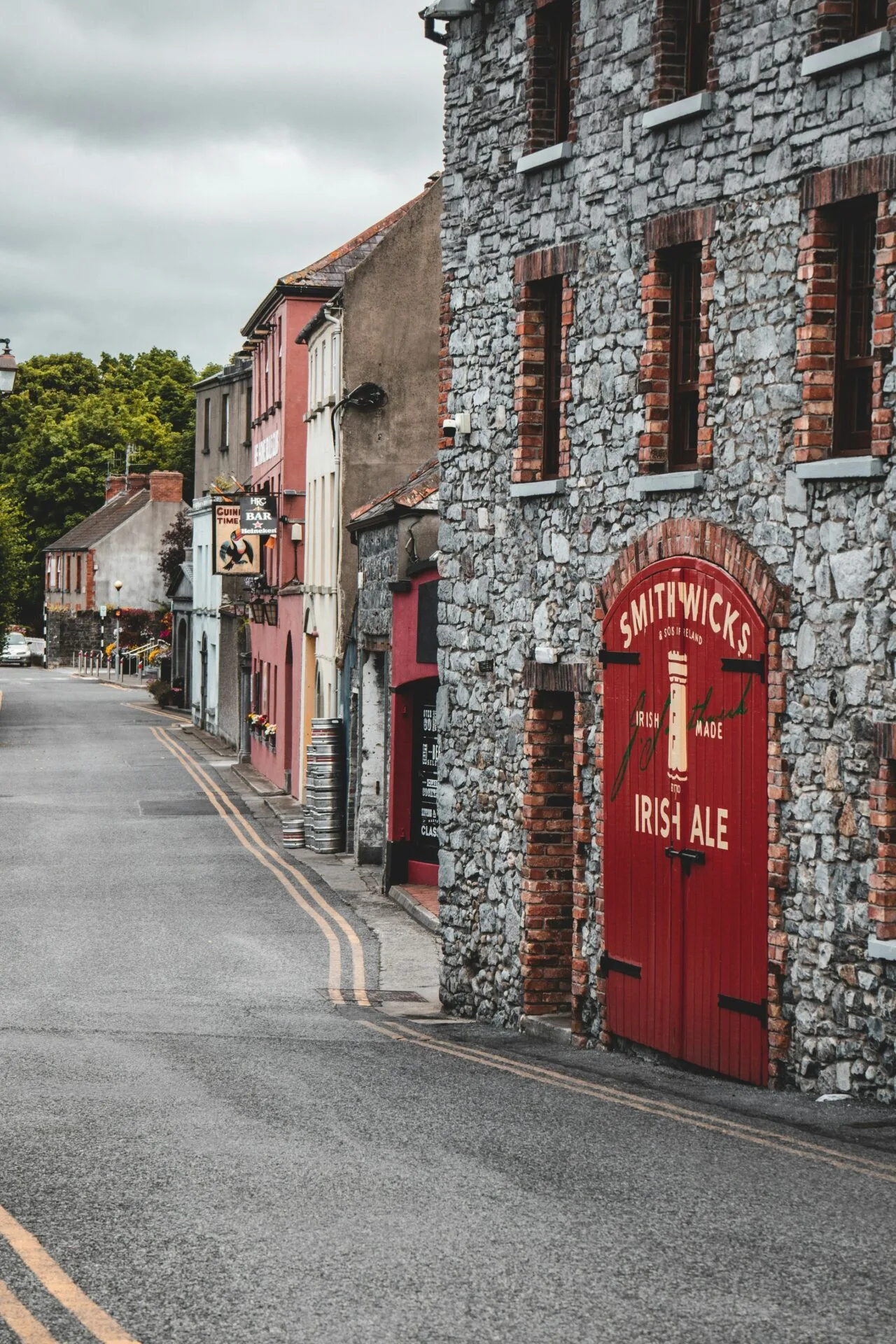A street shot of a KIlkenny street with shop fronts, pubs and a Smithwicks branded shed door